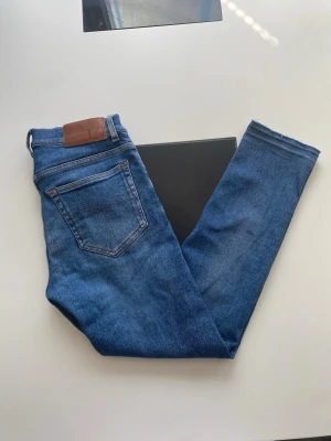 Blå slim jeans från Tiger of Sweden - Snygga blå slim jeans från Tiger of Sweden med klassisk femficksdesign och läderpatch bak i midjan. Jeansen har smal passform och är tillverkade i stretchigt denimtyg för en bekväm känsla. Perfekta till din vardagsstil.