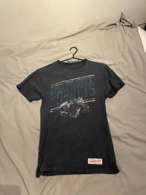 Vintage Mitchell & ness t-shirt - Säljer en svart Vintage t-shirt från Mitchell & Ness med Charlotte Hornets tryck framtill. T-shirten har rund hals, korta ärmar och en patch nertill. Perfekt för dig som gillar en chill look men ändå fet.