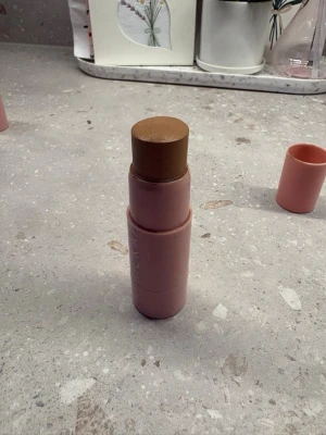 Bronzer stick Hickap - Krämig bronzer i stickformat från Hickap med en varm brun ton. Förpackningen är cylinderformad och ljusrosa, enkel att ta med i väskan. Perfekt för att skapa en solkysst look och enkel att applicera direkt på huden.