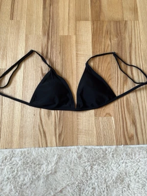 Svart trekantsbikini - Snygg svart trekantsbikini med tunna band i ryggen och nacken. Klassisk och stilren modell som passar perfekt till stranden eller poolen. Bikinin har en enkel design utan mönster och är fodrad på insidan.