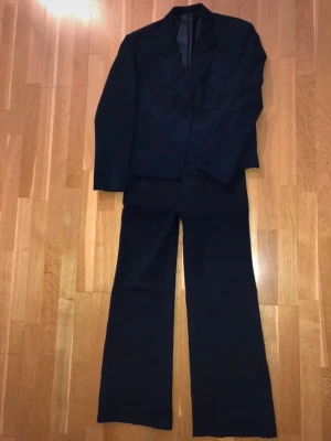 Filippa K Marinblå kostym med kavaj och byxor - Säljer en klassisk navy blue kostym med kavaj och raka kostymbyxori märket Filippa K. Kavajen har två fickor och knappar vid ärmslutet. Kostymen har en stilren och tidlös design, perfekt för dig som vill ha en snygg och enkel look. Ett minimal hål på undersidan/baksidan av vänstra ärmen men inget som går att fixas. Skriv vid fler bilder eller frågor. Nypris ca 7000kr
