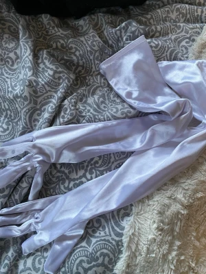 Långa vita satinhandskar - Säljer ett par eleganta, långa handskar i vit satin. De är släta och glansiga med en klassisk passform som går en bra bit upp på armen. Perfekta för en utklädnad eller liknande. 