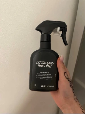 Lush Let The Good Times Roll Body Spray - En svart sprayflaska med body spray från Lush, Let The Good Times Roll. Flaskan rymmer 200 ml och har en modern, stilren design med vit text. Perfekt för dig som gillar doften av popcorn och vill ha något unikt i din parfymhylla.
