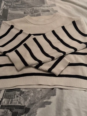 Vit stickad tröja med svarta ränder - Snygg vit stickad tröja med svarta horisontella ränder. Tröjan har rund halsringning och långa ärmar. Perfekt för dig som gillar en klassisk och stilren look. Materialet känns mjukt och bekvämt mot huden.