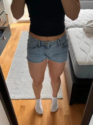 Lågmidjade ljusblå jeansshorts - Säljer ett par lågmidjade ljusblå jeansshorts med råa, fransiga kanter och klassiska femficksdetaljer. Shortsen har knapp och dragkedja framtill och är tillverkade i denim. Perfekta för sommarens alla äventyr!