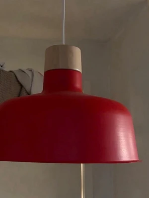 Röd taklampa i metall och trä - Snygg taklampa med rundad skärm i röd metall och detaljer i ljust trä. Lampan har en modern och stilren design som passar perfekt över matbordet eller i vardagsrummet. Hängs upp med vit sladd.