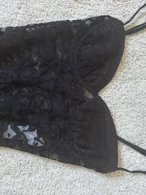 Svart spetsbody med tunna axelband - Snygg svart body i spets med blommigt mönster och tunna axelband. Bodyn har vadderade kupor och transparenta partier som ger en trendig look. Perfekt för dig som gillar stilrena och feminina underkläder.