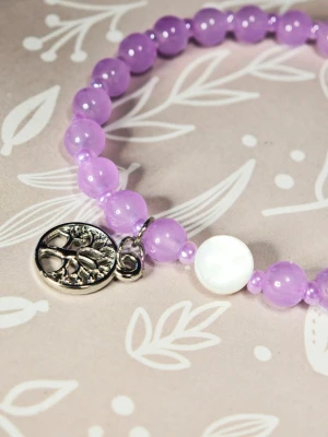 Lila pärlarmband med berlock - Snyggt armband med lila glas pärlor och en rund metallberlock med trädmotiv. Armbandet har även en vit, platt pärlemordetalj som kontrast. Perfekt accessoar för att addera färg till din outfit. Elastiskt armband av hög kvalitet, 18 cm långt.