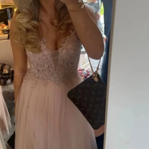 Ljusrosa balklänning med spetsdetaljer - Säljer en söt Rosa balklänning med gulliga detaljer. den är uppsydd så den passade mig som 155 när jag hade klackar, längden från banden vid axlarna är 140cm ner. Nypris är 3000 och att lägga upp kostade ca 1500. Märket är mascara. Den är bara använd en gång men saknar en av hasparna där bak men det är inget som märks, därav pris 
