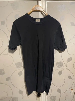 Svart basic t-shirt från KappAhl - En enkel svart t-shirt från KappAhl med rund halsringning och korta ärmar. Tillverkad i mjuk bomull för en bekväm känsla. Perfekt till jeans eller shorts för en clean och avslappnad stil.