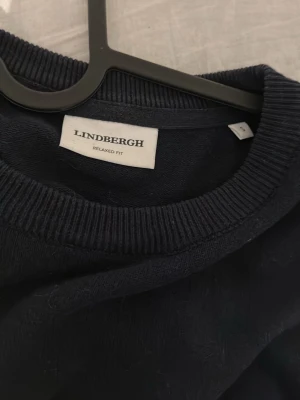 Mörkblå tröja från Lindbergh - Snygg mörkblå tröja från Lindbergh i relaxed fit. Tröjan har rund halsringning, långa ärmar och ribbade muddar vid ärmslut och nederkant. Perfekt basplagg som funkar till många olika stilar.