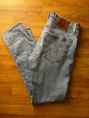 Levi's ljusblå raka jeans (Herr) - Säljer ett par klassiska ljusblå jeans från Levi's med raka ben och femficksmodell. Jeansen har den ikoniska läderpatchen bak i midjan och röd Levi's-tagg på bakfickan. Tillverkade i slitstark denim, perfekta för en avslappnad och tidlös look. Storlek w30/l32 