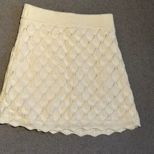 Beige stickad kortkjol med mönster - Supersöt beige stickad kortkjol med ett detaljerat rutmönster och vågig kant nertill. Kjolen har bred resår i midjan för skön passform och är perfekt för dig som gillar en mysig och trendig stil.