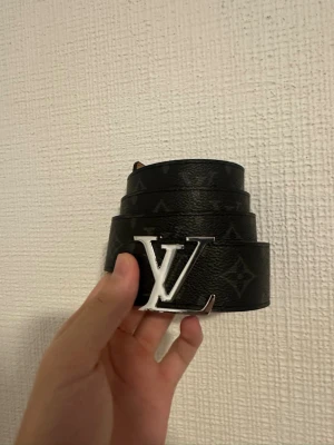 Svart bälte - Svart stilrent bälte i storlek 110 med silver badge 