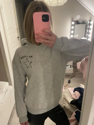 Grå hoodie med tryck Ma Chérie - Säljer en ljusgrå hoodie från gina tricot med svart tryck där det står 'Ma Chérie' och en stjärna både fram och bak. Det finns inga tecken på användning men den har kommit till användning men inte längre, därför jag säljer den. 