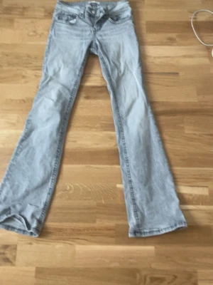 Gina tricot jeans - Säljer ett par ljusgrå bootcut jeans med snygga bakfickor som har lock och knappdetaljer. Jeansen har klassisk femficksmodell, bälteshällor och är tillverkade i mjukt denimtyg. Perfekta för en avslappnad och trendig look. Köpt från gina för 1 år sen men kanppt använda🩶🩶