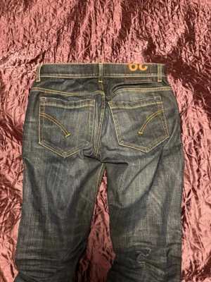 Mörkblå jeans från Dondup - Säljer ett par mörkblå jeans från Dondup med klassisk femficksmodell och kontrastsömmar. Jeansen har raka ben och snygga detaljer på bakfickorna med gul söm. Perfekta till sneakers och t-shirt för en avslappnad look. Modell George men lappen är borta
