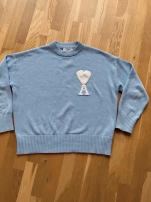 Ljusblå stickad tröja Ami Paris - Säljer en ljusblå stickad tröja från Ami Paris med deras ikoniska vita hjärta och bokstaven A på bröstet. Tröjan har rund hals, ribbade muddar och nederkant. Perfekt för dig som gillar stilrena och trendiga plagg. Går att diskutera pris!
