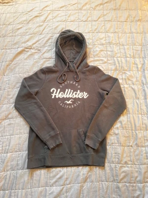  hoodie från Hollister - Snygg mörkgrå hoodie från Hollister med stor vit logga och texten 'Southern California' på bröstet. Hoodien har huva med dragsko, känguruficka och ribbade muddar vid ärmar och nederkant. Perfekt för en avslappnad och cool stil.  Pris kan diskuteras !