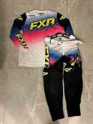 FXR Race Div motocross set - Säljer ett fett motocross set från FXR Race Div med långärmad tröja och byxor. Färgerna är en mix av vit, svart, blå, rosa och neon-gul med stora FXR-loggor. Materialet är lätt och ventilerande, perfekt för intensiva race och träning. Det är påtryckt namn och nummer i back vilket gör att priset sänks. Nypris på byxorna och tröjan tillsammans är 1500kr! Skriv om ni har minsta lilla fråga! 
