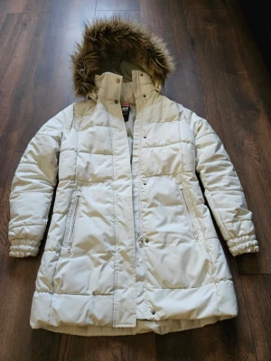 Helly Hansen vinterjacka - Helly Hansen vinterjacka i mycket fint skick. Varm och bekväm längre modell med huva och pälsdetalj, perfekt för kalla vinterdagar. Klassisk och tidlös design i ljus beige/vit färg som passar till allt. Jackan är lätt men varm och fungerar bra både till vardags och under kallare väder. Endast använd ett fåtal gånger och väl omhändertagen. Storlek S (Regular fit). Säljs då den inte längre används.