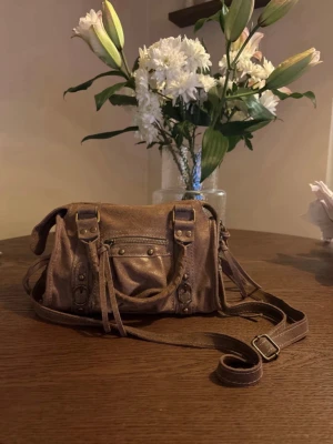 Brun väska  - Säljer tyvärr min axelrems/handväska ifrån Italien👜☀️ Väskan har guldiga detaljer och justerbart/avtagbart axelband. Säljer på grund av att jag köpte två liknande, och inte får användning för båda!💞