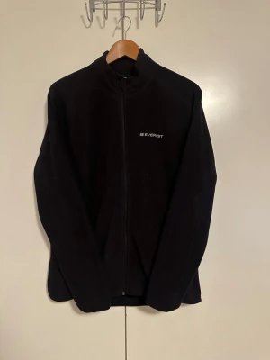 Vintage Svart fleece från Everest - Mjuk och skön svart fleecejacka från Everest med dragkedja framtill och diskret logga på bröstet. Jackan har hög krage och långa ärmar, perfekt för lager-på-lager och chill dagar. Passar M/L
