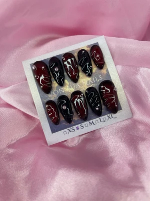 Monster (S);Medium Almond - Snygga handgjorda press-on naglar i svart och vinrött med handmålad monster logo och små silverfärgade stenar. Naglarna har en medium mandelformad design och en glansig finish som ger en cool och edgy look. Perfekt för dig som vill sticka ut med unika detaljer.S: 15 mm, 11,5 mm, 12 mm, 11 mm, 9 mm 