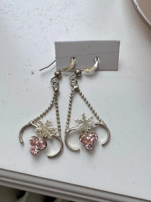 Vackra unika örhängen med detaljer - Unika vintage silvriga/vita örhängen med hängande kedjor, snöflingeformad detalj och tre ljusrosa diamanter i kluster. Aldrig sett något likande🩷Örhängena har en halvmåneformad design och är tillverkade i metall med glittrande diamanter som ger en elegant och vacker look!!😻De är lätta att ta in och ut, och sitter kvar med plast pluppar baktill! Använts en gång av mig men köptes secondhand, jag är känslig och fick ingen reaktion mot dom så de går att använda❣️De har inga defekter heller! 