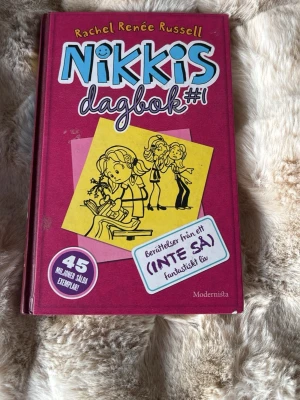 Nikkis dagbok #1 av Rachel Renée Russell - Nikkis dagbok #1 är en ungdomsbok av Rachel Renée Russell med hårda, vinröda pärmar och färgglad framsida. Boken handlar om Nikki och hennes vardag, vänskap och pinsamheter. Perfekt för dig som gillar humor och dagboksstil.