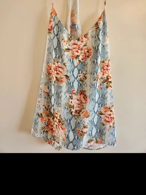 Blommig linnetopp från Single Los Angeles, stl XL  - Säljer en snygg linnetopp från Single Los Angeles med tunna axelband. Toppen har ett unikt mönster med stora rosa och orange blommor mot en vit och blå bakgrund med mönster. Perfekt för dig som vill sticka ut med en cool och somrig vibe.