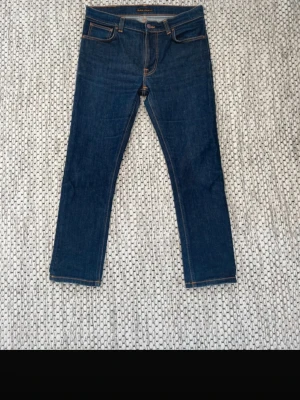  Nudie Jeans lean dean - 33w 30l Snygga mörkblå jeans från Nudie Jeans med klassisk femficksmodell och kontrastsömmar. Raka ben och normal midja. Tillverkade i slitstark denim med Nudie-logga på bakfickan. Perfekta för en clean och stilren look. 