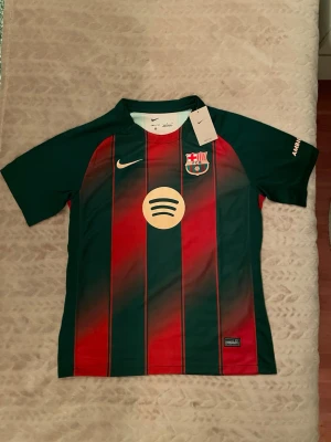 FC Barcelona matchtröja Nike - Snygg FC Barcelona matchtröja från Nike med klassiska röd-blå vertikala ränder, klubbmärke på bröstet och Spotify-logga i mitten. Tröjan har korta ärmar och är tillverkad i ett lätt och ventilerande funktionsmaterial, perfekt för fotbollsträning eller match.