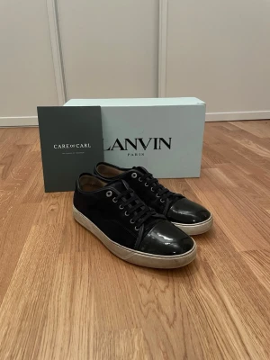 Svarta sneakers från Lanvin - Snygga svarta sneakers från Lanvin med klassisk design. Skorna har en kombination av mocka och glansigt skinn på tån, vita sulor och svarta snören. Perfekta för dig som gillar stilrena och exklusiva sneakers.