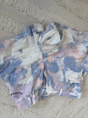 Pastellfärgade tie-dye shorts - Unika shorts i pastellfärgat tie-dye-mönster med blå, lila och rosa toner. Modellen har hög midja, fickor bak och knappar framtill. Använd fåtals gånger.Vet dock inte varför bilderna blev upp och ned. Ord pris 300kr