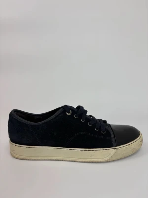Mörkblå Lanvin sneakers med lackad tå - Snygga mörkblå sneakers med ovandel i mocka och svart lackad tå. Skorna har vita sulor och klassisk snörning med metallöljetter. Perfekta för dig som gillar en stilren men ändå unik look.