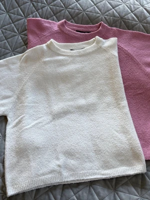 Två stickade tröjor i vitt och rosa - Två stickade tröjor, en vit och en ljusrosa. Rund halsringning, halvlånga ärmar och rak passform. Lätta och bekväma.