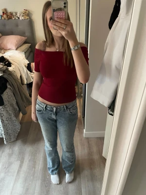 Mörkröd offshoulder topp - Trendig mörkröd offshoulder topp med tight passform och korta ärmar. Toppen är croppad och tillverkad i mjuk bomull, perfekt för en snygg och enkel look. Snygg att matcha med jeans eller kjol.