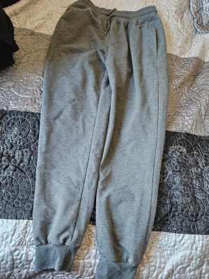 Grå mjukisbyxor med resår - Gråa mjukisbyxor med resår i midjan och vid bensluten. Byxorna har dragsko i midjan och sidofickor. Perfekta för chill eller träning. Mjukt och bekvämt material i klassisk modell.