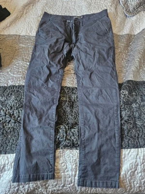 Mörkgrå chinos från Dressmann - Snygga mörkgrå chinos från Dressmann med klassisk rak passform. Byxorna har sidfickor och är tillverkade i mjukt bomullstyg. Perfekta för en stilren och avslappnad look.