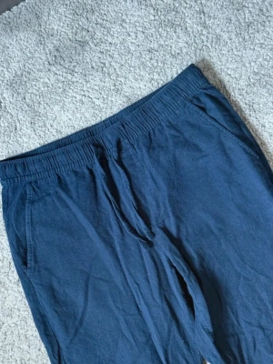 Mörkblå linnebyxor  - Riktigt snygga mörkblå linnebyxor med elastisk midja och snörning framtill. Storlek S. Byxorna har raka ben, sidfickor och två bakfickor. Perfekta för chill dagar eller när du vill vara bekväm. Tillverkade i mjukt bomullsmaterial som känns skönt mot huden.