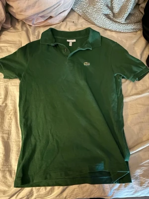 Lacoste piké  - Säljer pga används inte. Den är i bra skick. Den är i junior storlek, 176cm syns på bild men passar lätt xs-s. Jag är 178 och den passar mig. Skriv om fler bilder med bättre ljus önskas.