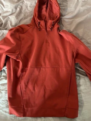 Röd hoodie från Puma med dragkedja - Snygg röd hoodie från Puma med halv dragkedja framtill och justerbar huva med snören. Hoodien har en sportig look och en stor ficka framtill. Perfekt för dig som gillar streetwear och vill ha något bekvämt och stilrent.