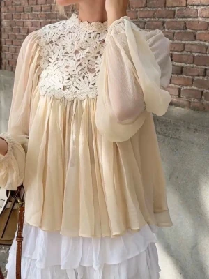 Beige blus med spetsdetaljer - Romantisk beige/cremefärgad blus i tunn chiffong med långärmade puffärmar och vackra virkade spetsdetaljer över bröst och axlar. Blusen har en lös, flowy passform och knäppning bak i nacken. Perfekt för dig som gillar en bohemisk och feminin stil. Finns en fläck på ärmen som knappt syns. Blusen är ny med prislapp