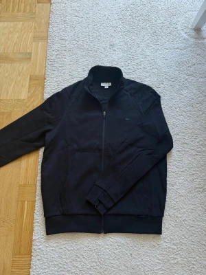 Svart zip-hoodie från Lacoste - Snygg svart hoodie från Lacoste med dragkedja framtill och diskret logga på bröstet. Nypris 1900kr på Zalando!  Finns ej i sortiment längre!