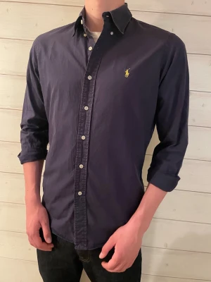 Mörkblå skjorta från Ralph Lauren - Klassisk mörkblå skjorta från Ralph Lauren. Skjortan är i fint skick i storlek M.                           Skriv om ni undrar något eller har några frågor!