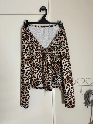 Leopardmönstrad topp med knyt - Trendig långärmad topp med leopardmönster och snygg knytning framtill. Djup v-ringning och figurnära passform gör den perfekt för en cool och edgy stil. Tillverkad i mjukt och stretchigt material för extra komfort. Inte säker på storleken men skulle själv säga xs - xxs 