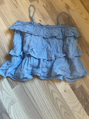 Ljusblå volangtop från Gina Tricot - Söt ljusblå linnetopp från Gina Tricot med tunna axelband och flera volanglager. Toppen är luftig och har en flowy passform som ger en avslappnad och trendig look. Perfekt för varma dagar och enkel att styla med jeans eller kjol. Ny pris runt 250kr tror jag. Kontakta för att diskutera mitt pris .