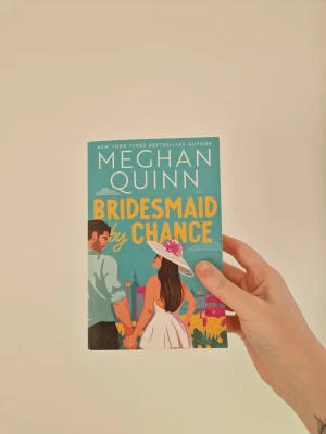 Bridesmaid by Chance av Meghan Quinn - En färgstark pocketbok med titeln 'Bridesmaid by Chance' av Meghan Quinn. Omslaget är turkost med illustration av ett par som håller varandra i handen, där kvinnan bär en vit klänning och hatt med blomma. Perfekt för dig som gillar romantisk feelgood. Läst en gång. Defekter syns på bilderna