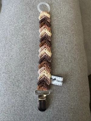 Virkad napphållare  - Virkad, flerfärgad napphållare i brunt/beige. Virkad av mig i 100% bomullsgarn med metallclip och silikonring.  Mönsterskapare: animo.design